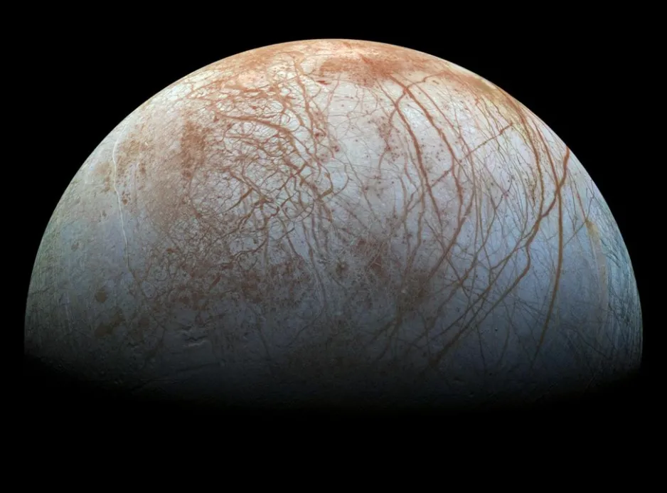 A grey hemisphere of Europa showing a pattern of orange sinuous lines and fractures crisscrossing the moon’s surface, all against a black background.