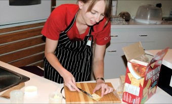A woman wearing a red shirt and black-and-white striped apron spreads butter on a cracker.