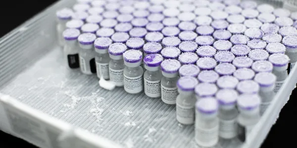 Dozens of tiny vials of vaccine sit side-by-side in a square tray