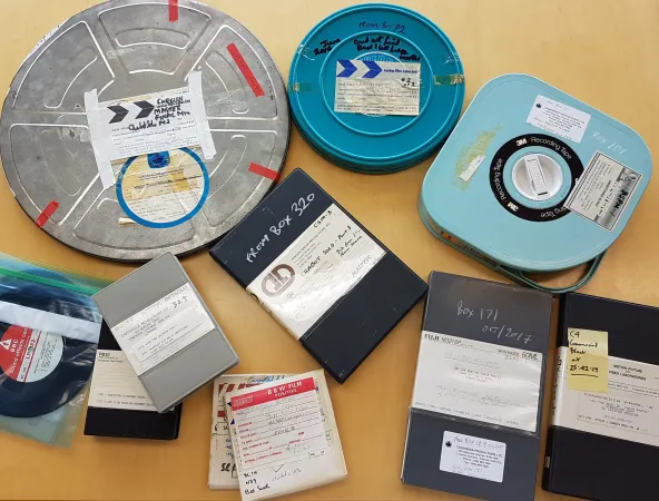 Divers formats audiovisuels, dont des films, des cassettes audio et différents types de cassettes vidéo, provenant du Fonds Les Harris, sont étalés sur une table. 