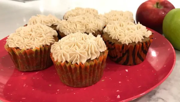 A close-up depicts a red plate filled with cupcakes. Two apples sit next to the plate.