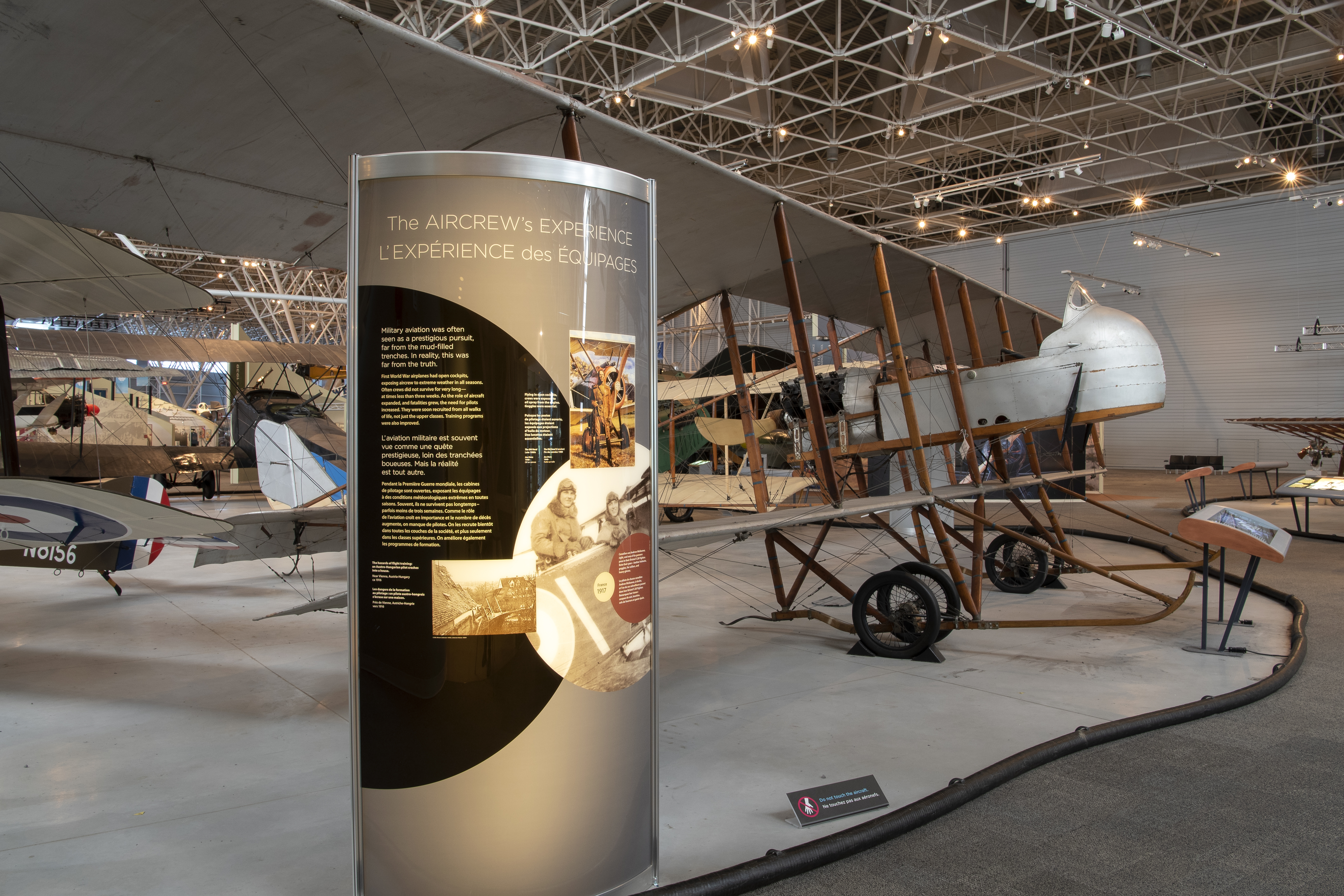 A sleek-looking panel stands in the foreground; in the background several aircraft are visible on the floor of the Canada Aviation and Space Museum.