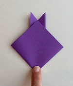 Square purple paper in diamond shape. Two triangular ears stick up above the head.
