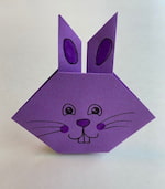 Purple origami rabbit with a smiling face coloured in fine marker.