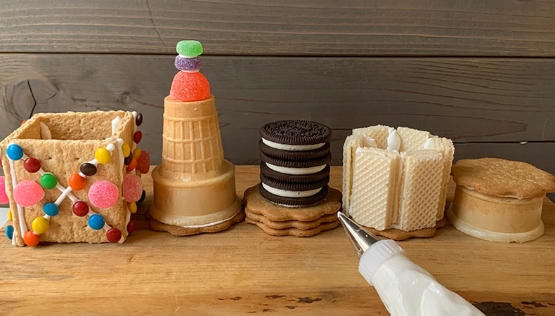 Five pre-assembled sections of the rocket, made with cookies and candies, sit on a wooden surface along with a piping bag of royal icing.