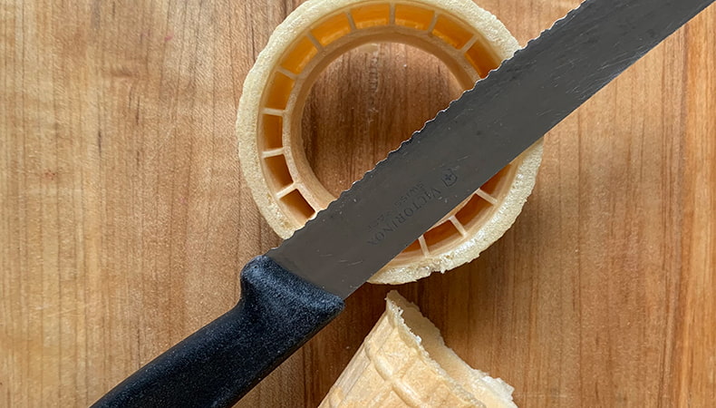 Un couteau repose sur le dessus d’un cornet de crème glacée gaufré qui a été coupé en deux à l’horizontale.