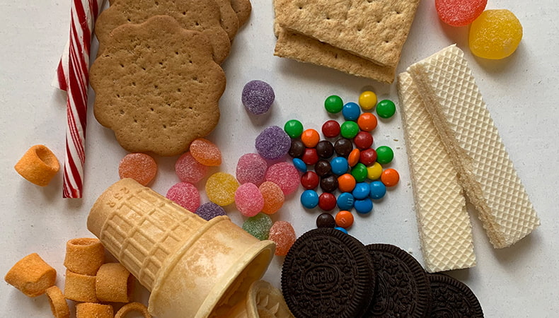 Un assortiment de biscuits et de bonbons nécessaires pour la recette repose sur une surface blanche unie.