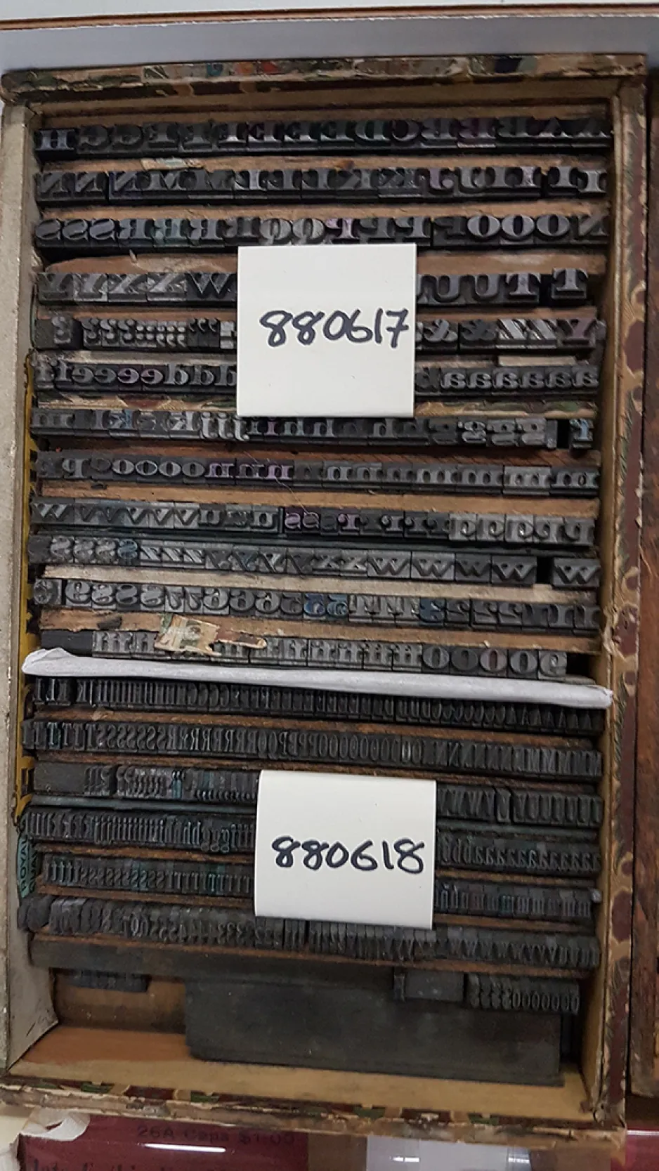 Two artifacts housed in a wooden box. They are made up of foundry type that are organized alphabetically right to left. The first artifact is labeled with a white tag with black writing that says “880617.” It is a 16-point display typeface with serifs on the characters. The second artifact is labeled with a white tag with black writing that says “880618.” It is a 16-point condensed typeface with serifs.