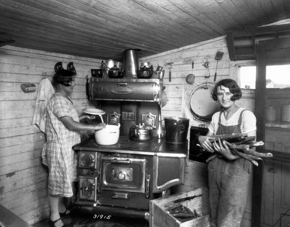 Preparing dinner on a wood stove in the First House, St Jean-Baptiste MB 