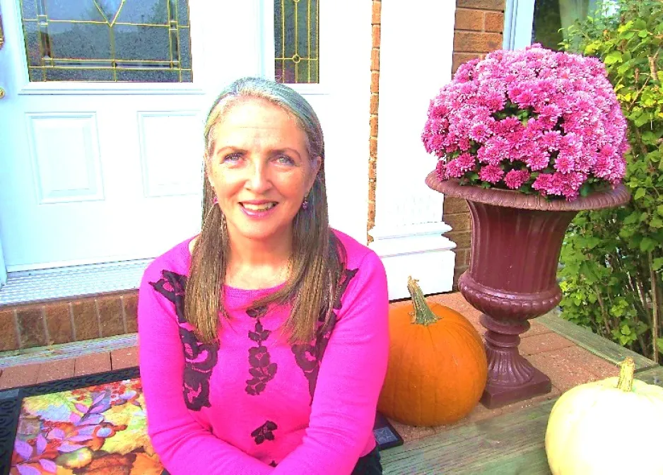 Dawn Nicholson-O’Brien, assise sur le pas d’une porte, à côté d’un pot de fleurs roses.