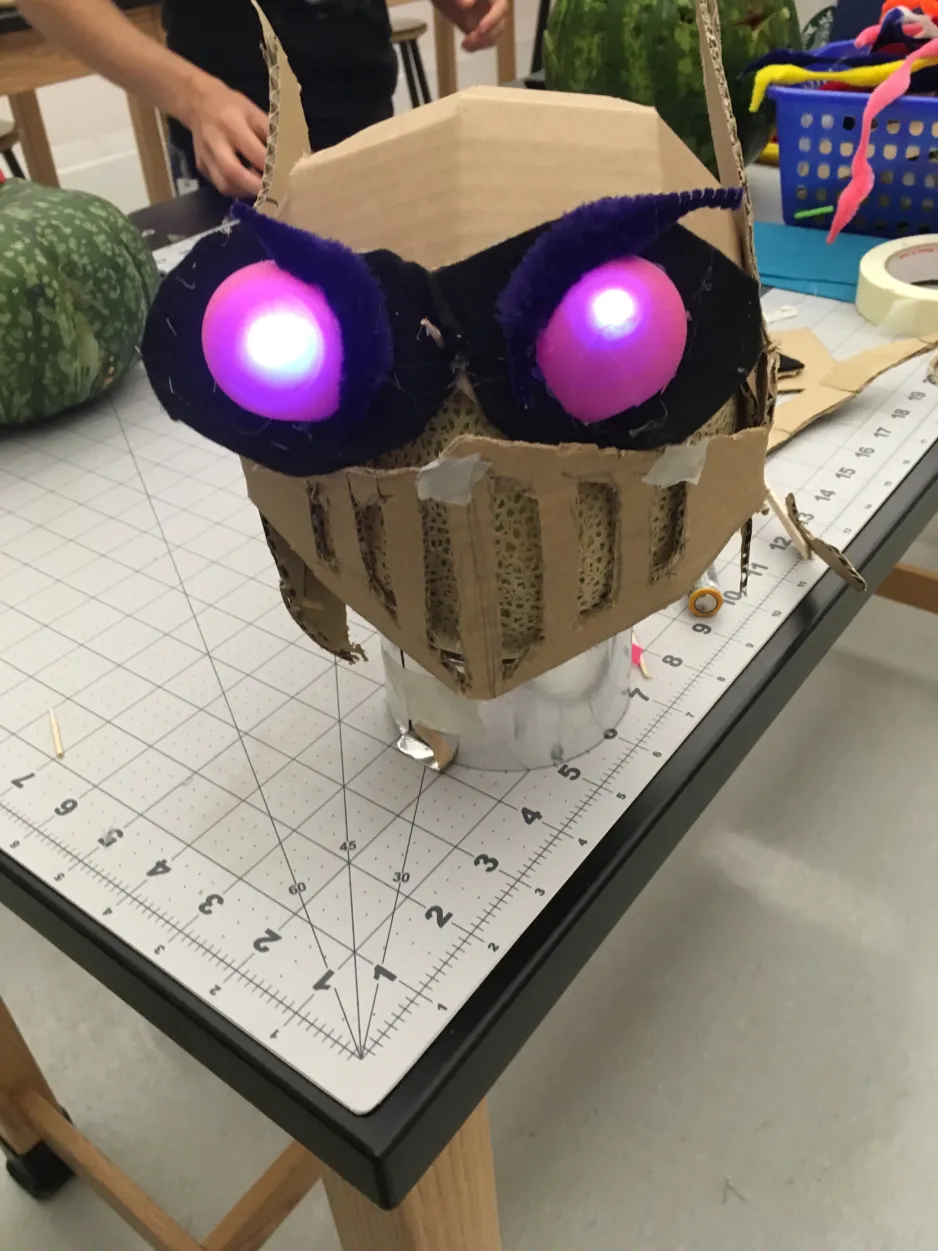 A cantaloupe wearing light-up eyes and a cardboard helmet  