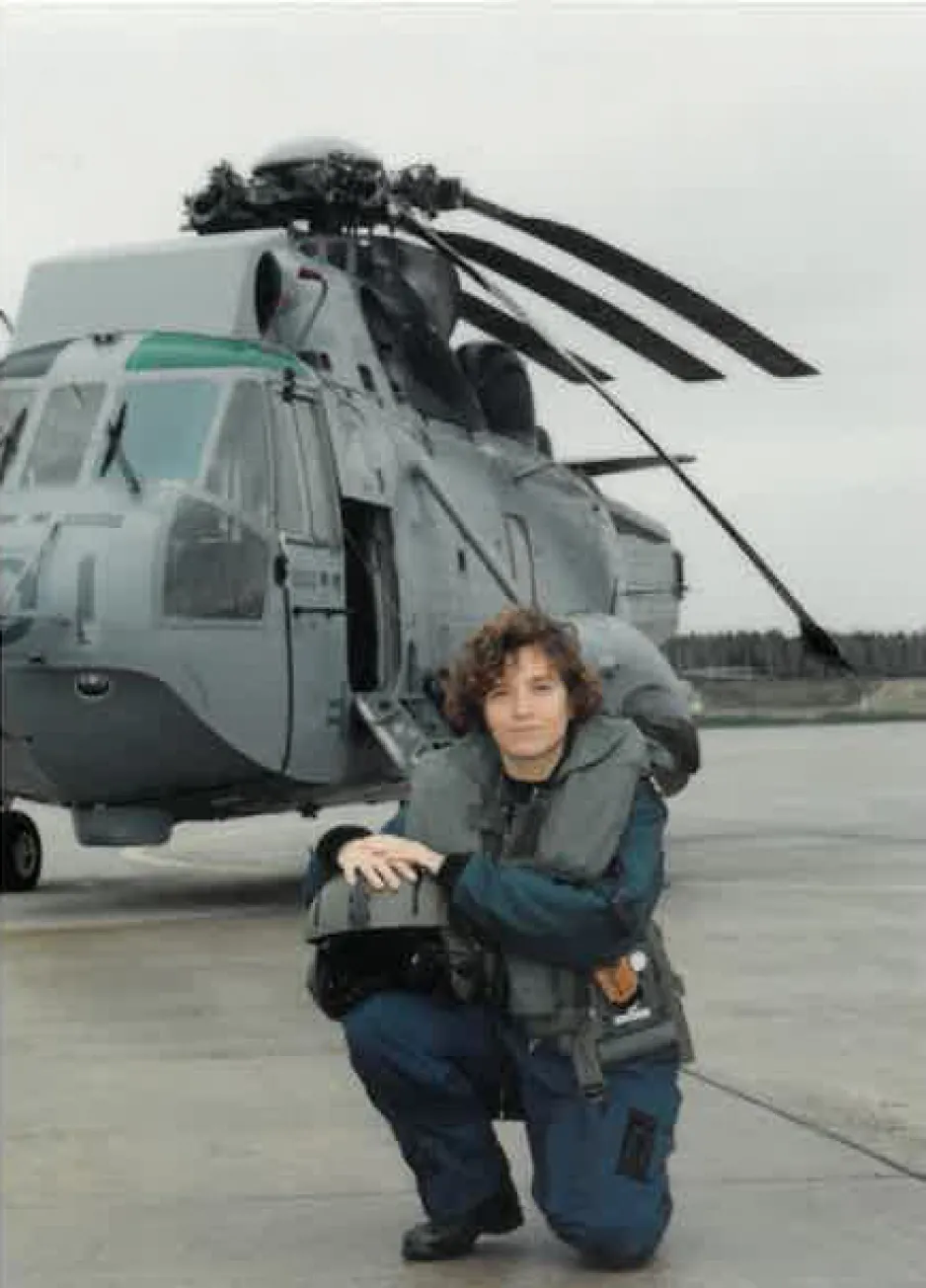 A woman in a blue military uniform poses in front of a large helicopter.