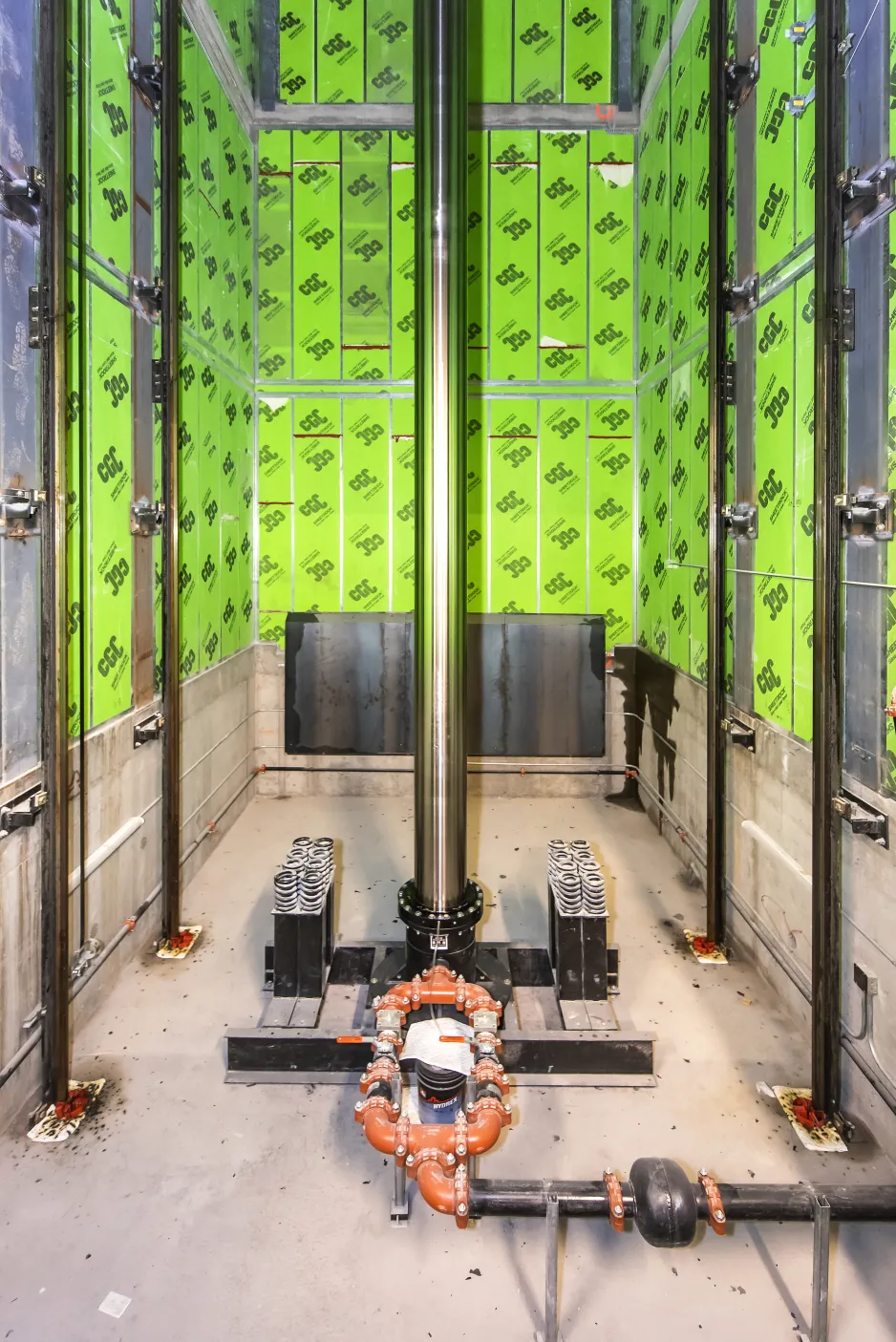 Vue de l’intérieur de la cage du monte-charge, qui est un volume rectangulaire aux murs vert vif et au centre duquel s’élève une gigantesque colonne en acier.