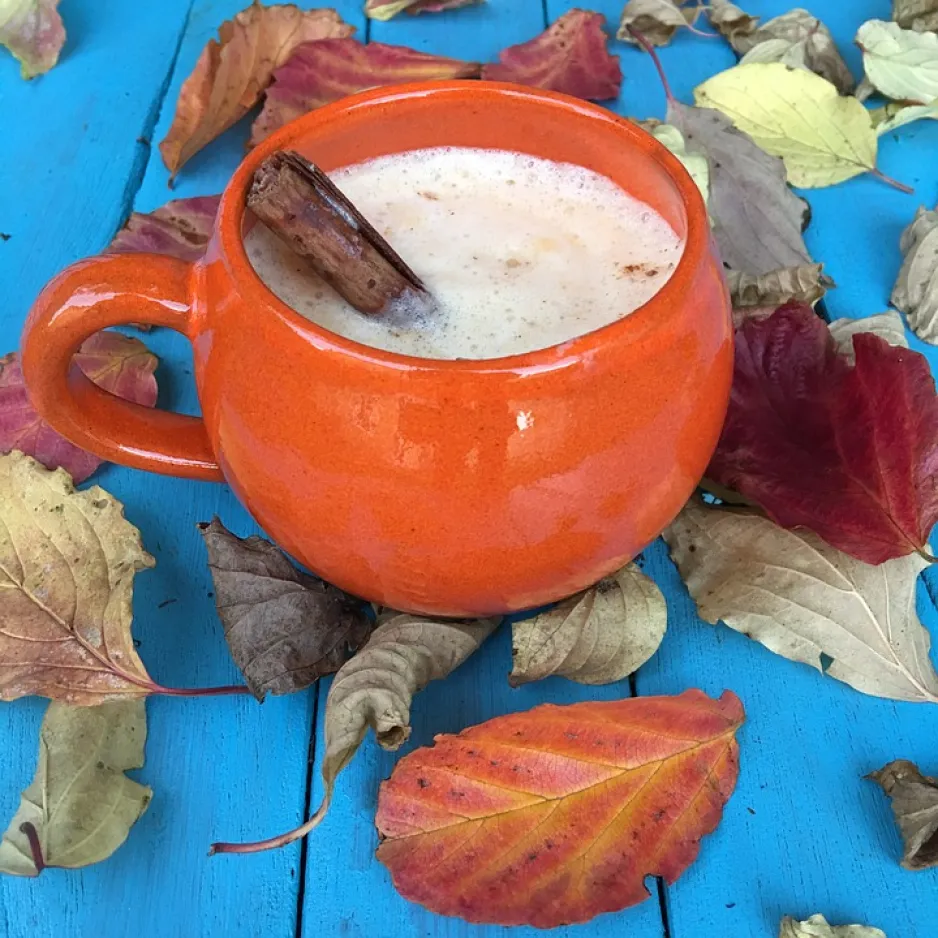 A mug filled with pumpkin spice latte, sitting on an outdoor table surrounded by fall leaves.