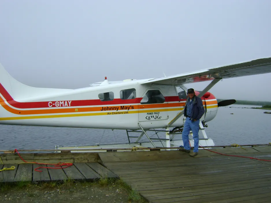 Le pilote se tient debout à côté d’un petit aéronef blanc flottant sur l’eau près d’un quai.