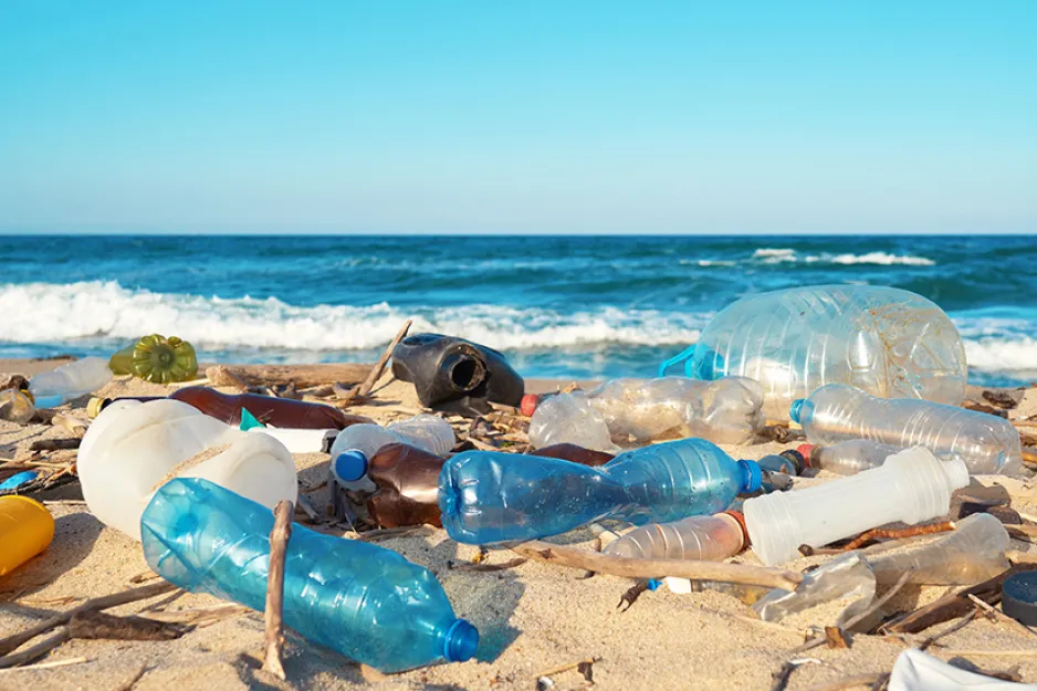 Plastic waste litters a sandy beach, with an ocean visible in the background.