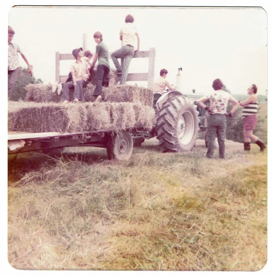 Une ancienne photo montre des enfants profitant d’une promenade en chariot de foin tiré par un tracteur. 