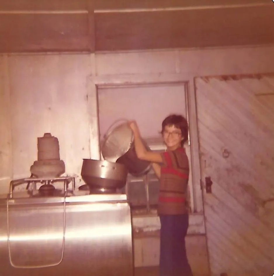 An old image shows a young girl pouring milk out of a large, silver bucket and into a tank.