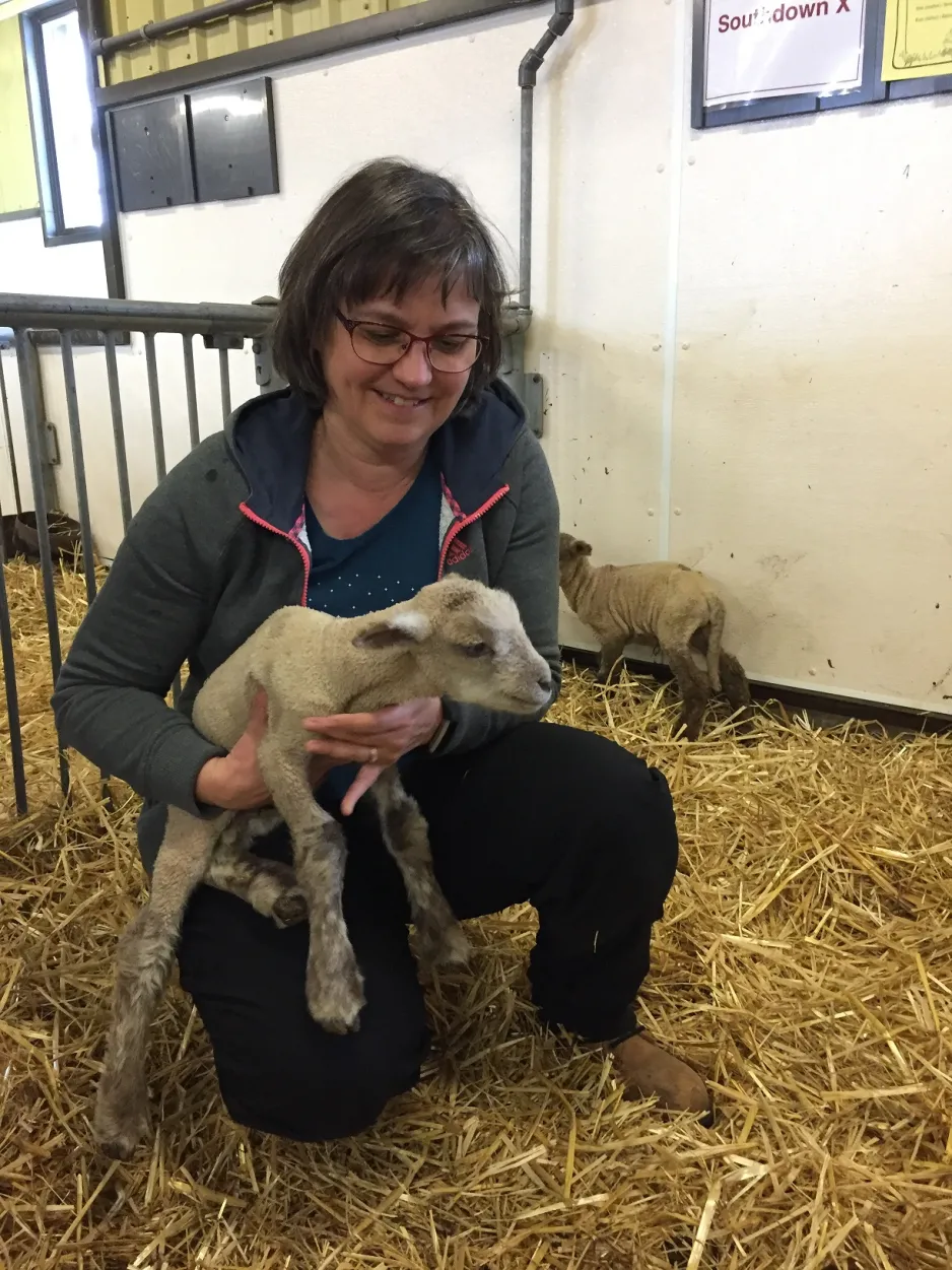 Une femme sourit en tenant dans ses bras un agneau qui vient de naître. 