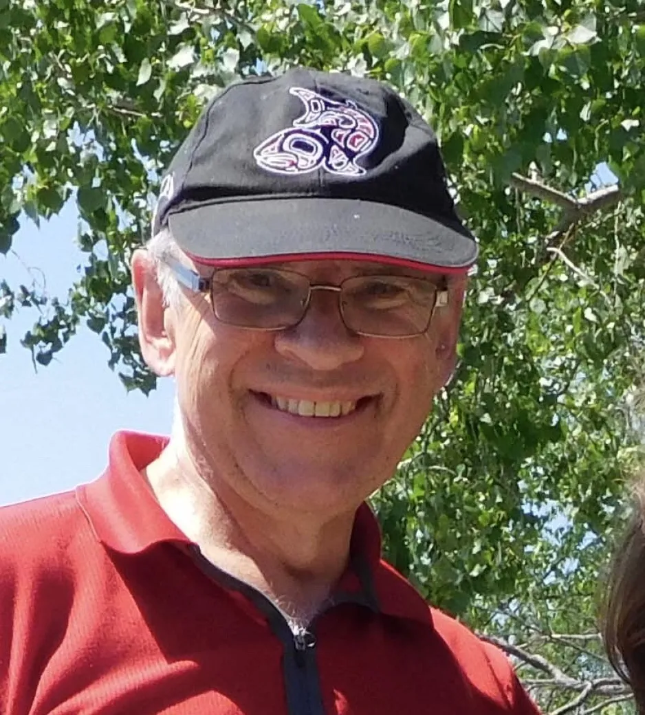 A man in a red shirt and ball cap smiles warmly at the camera.