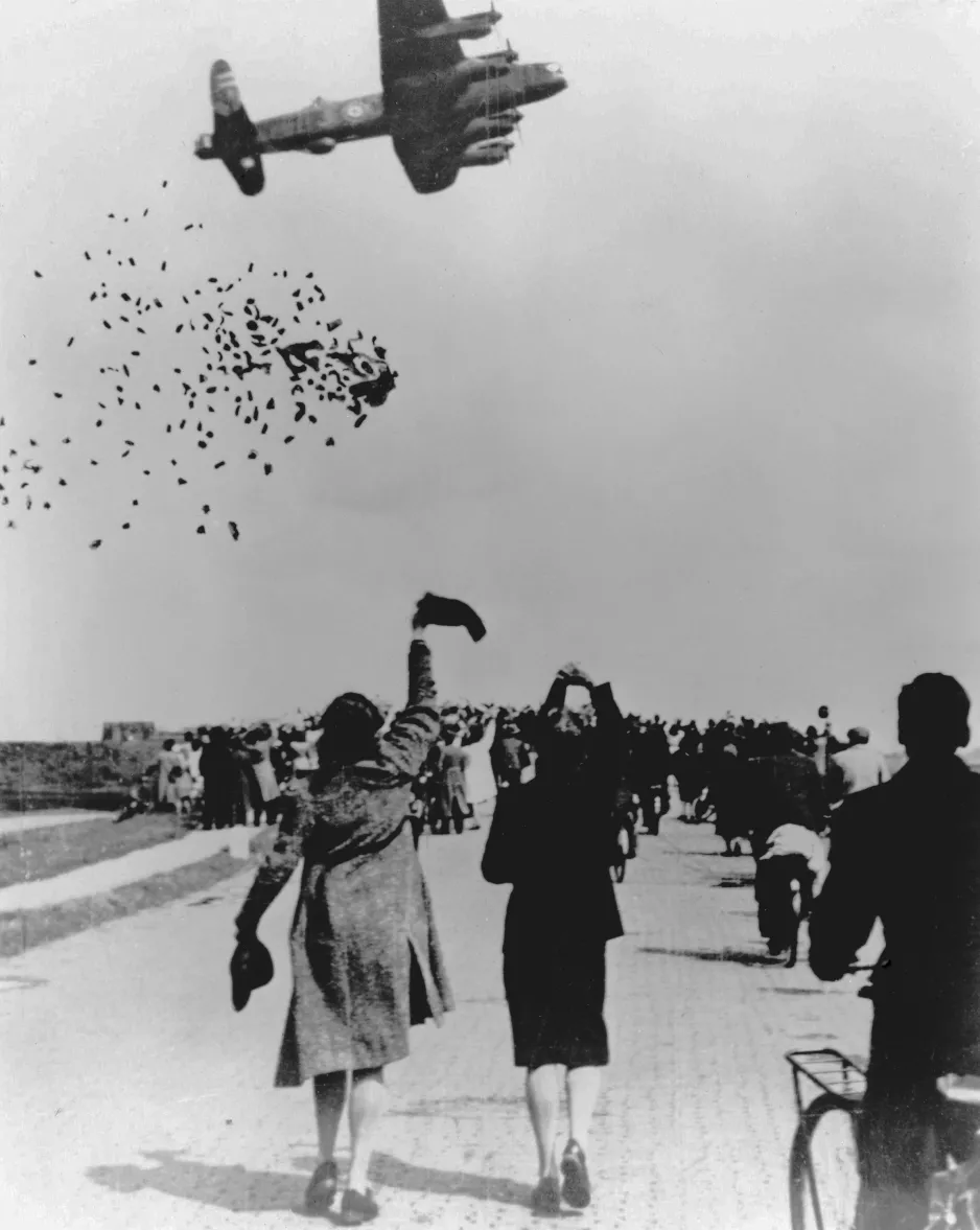 A black-and-white image depicts food packages falling from a low-flying aircraft; people are running towards the falling cargo. Wikimedia Commons