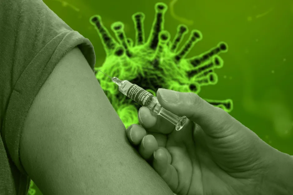 A vaccine is injected into the arm of a patient. In the background is an image of a coronavirus.
