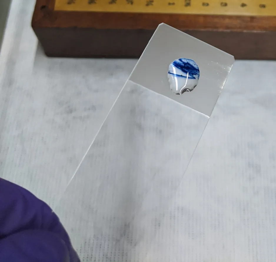 Vue rapprochée d’une petite goutte de liquide blanc et bleu sur le bout d’une lame en verre; il s’agit d’un exemple de résultat positif d’un test à la diphénylamine.