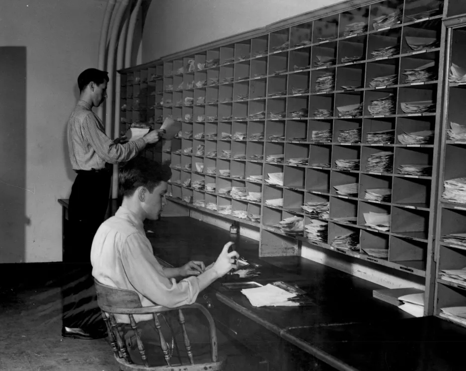 Sur une photo historique en noir et blanc, deux jeunes hommes classent le courrier dans un casier.