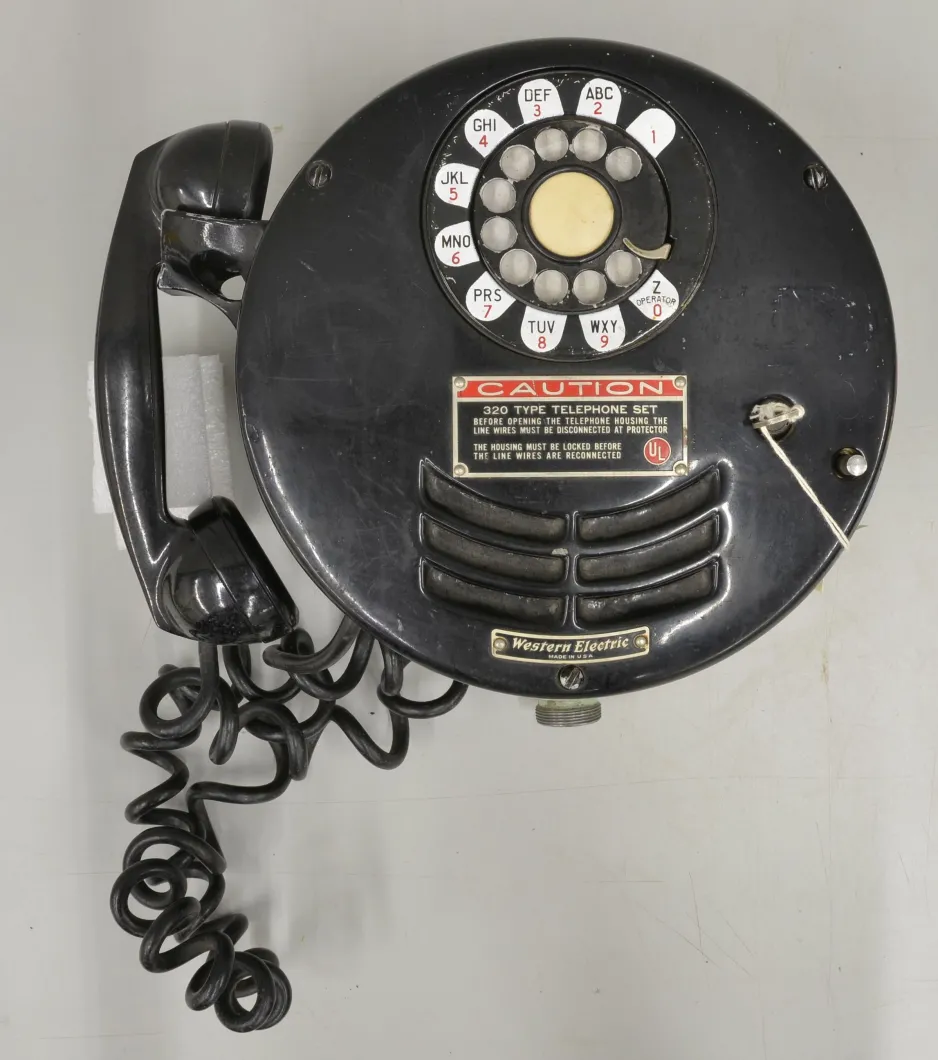 Un appareil téléphonique pour mine rond, à cadran et en métal peint en noir, repose sur un fond gris.