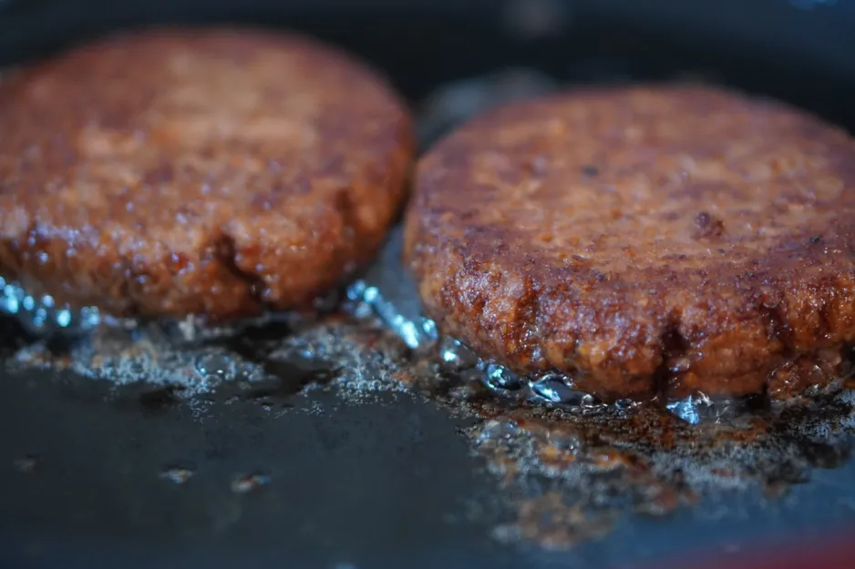 A close-up image of two burger patties cooking in a pan.