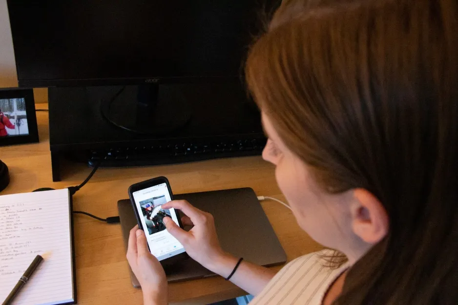 Une jeune femme regarde un téléphone intelligent, dont l’écran montre une personne tenant un poisson. La photo a été prise par-dessus l’épaule de la jeune femme.
