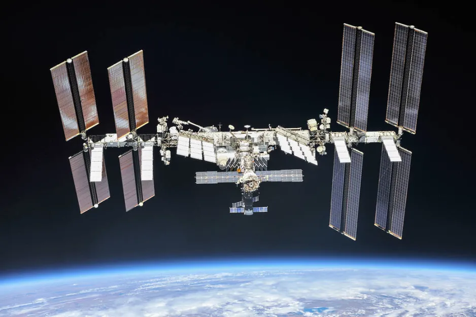 The International Space Station is centre in the image, with black space above it and the blue Earth below it.