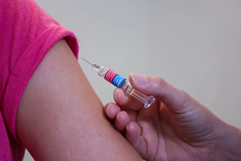 Gros plan d’une main avec une seringue s’apprêtant à vacciner une personne.