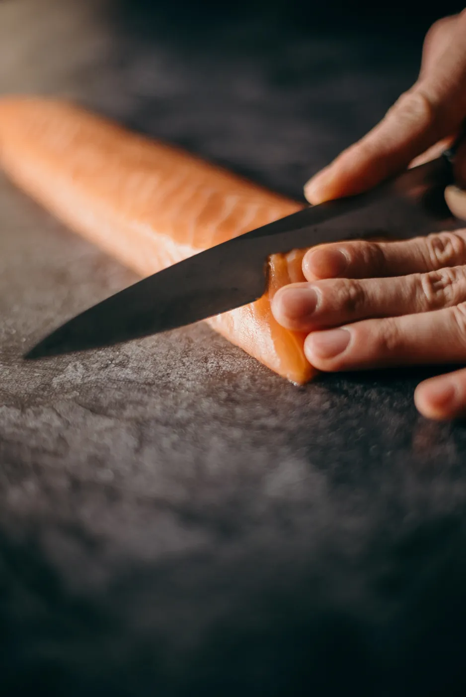 A hand holding a knife, carefully slicing a salmon filet. 