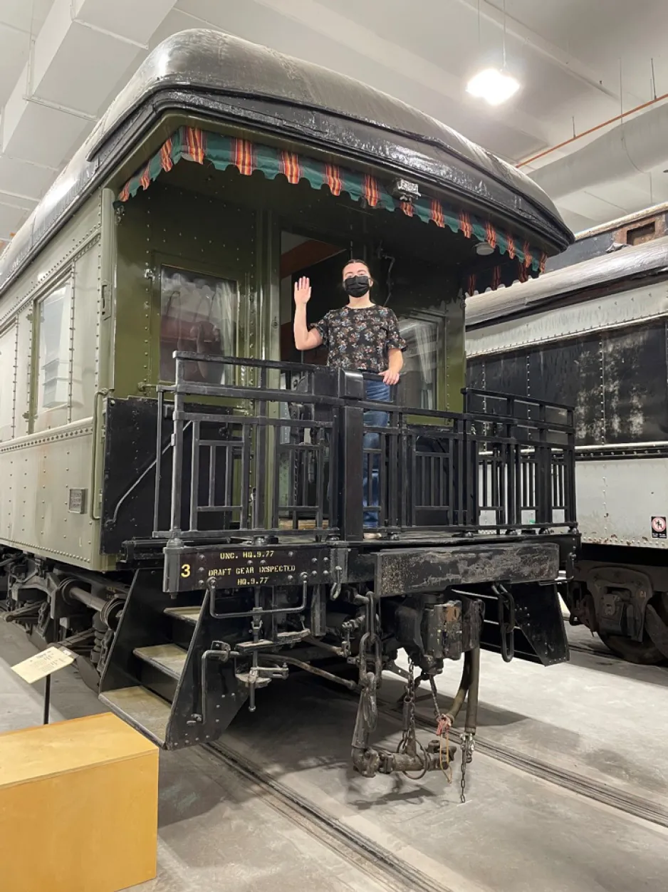 A woman standing on a rail car’s metal platform and waving. 