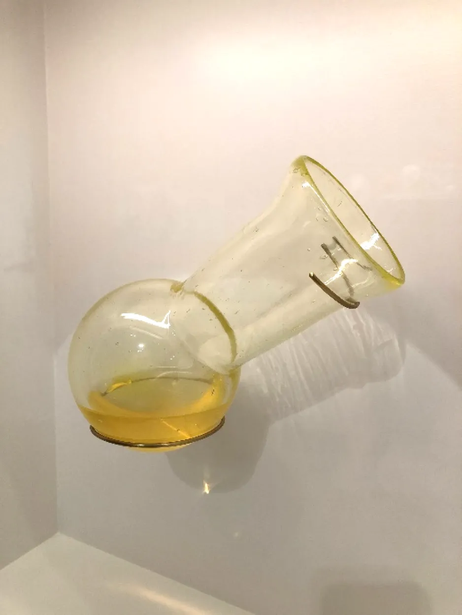 A clear glass round-bottomed flask sitting against a white background with a yellow liquid in the bottom.