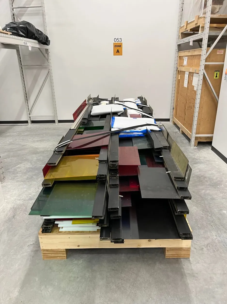 Wooden pallets carrying yellow, green, and red pieces of plexiglass in a large storage room.