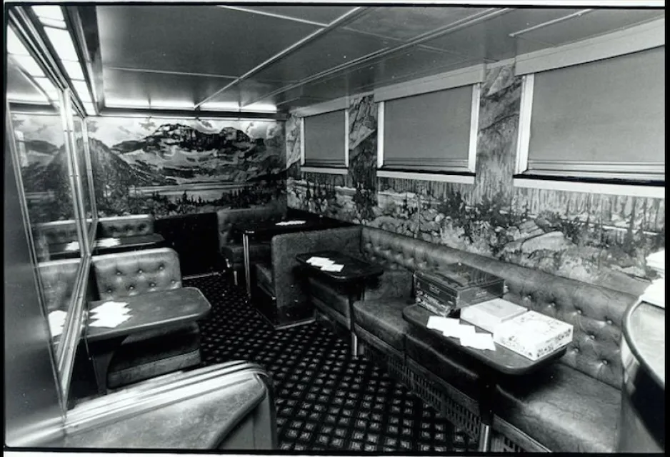 A black-and-white image depicts the inside of a train car; the walls are decorated with detailed landscape paintings.