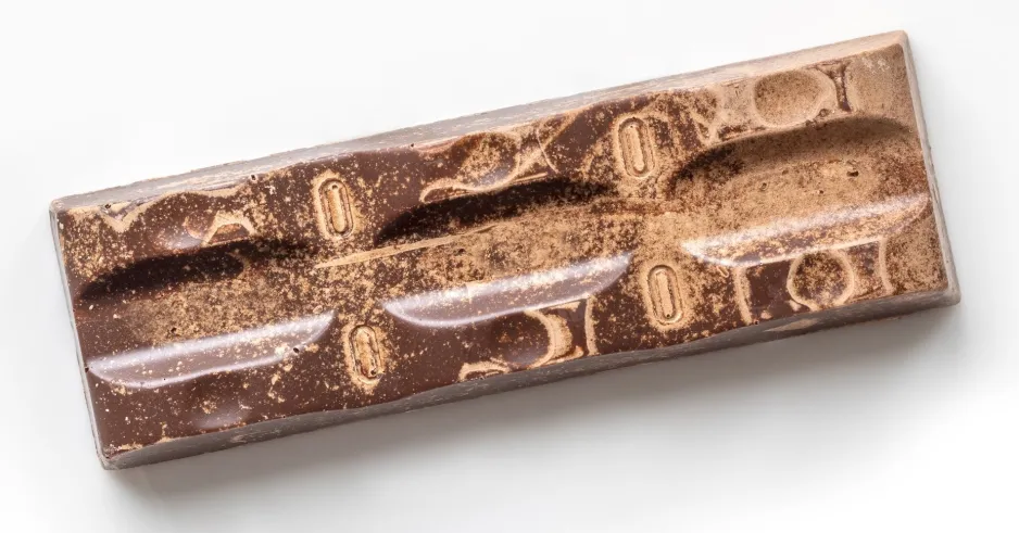On voit une barre de chocolat sur un fond blanc qui a des taches plus pâles démontrant des signes qu’elle a dépassé sa durée de conservation. 