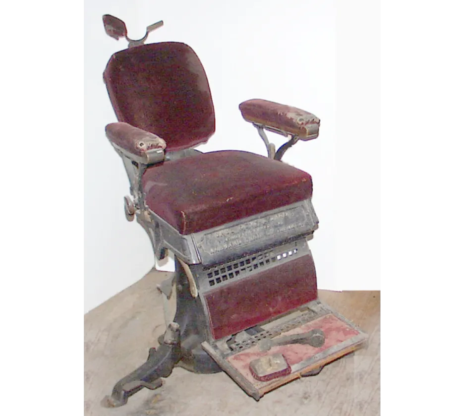 An old dental chair is covered in a dark red upholstery, and appears to be covered in dust.