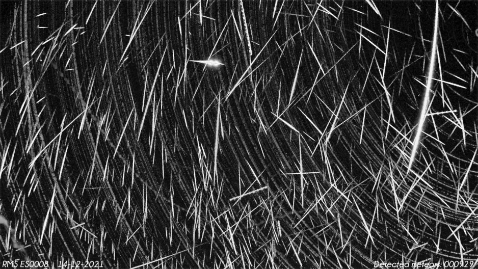 Des centaines de traînées blanches représentant des météores, dont la plupart sont allongées le long du bas de l’image, sur un fond noir, et de fines lignes radiales blanches représentant le mouvement des étoiles.