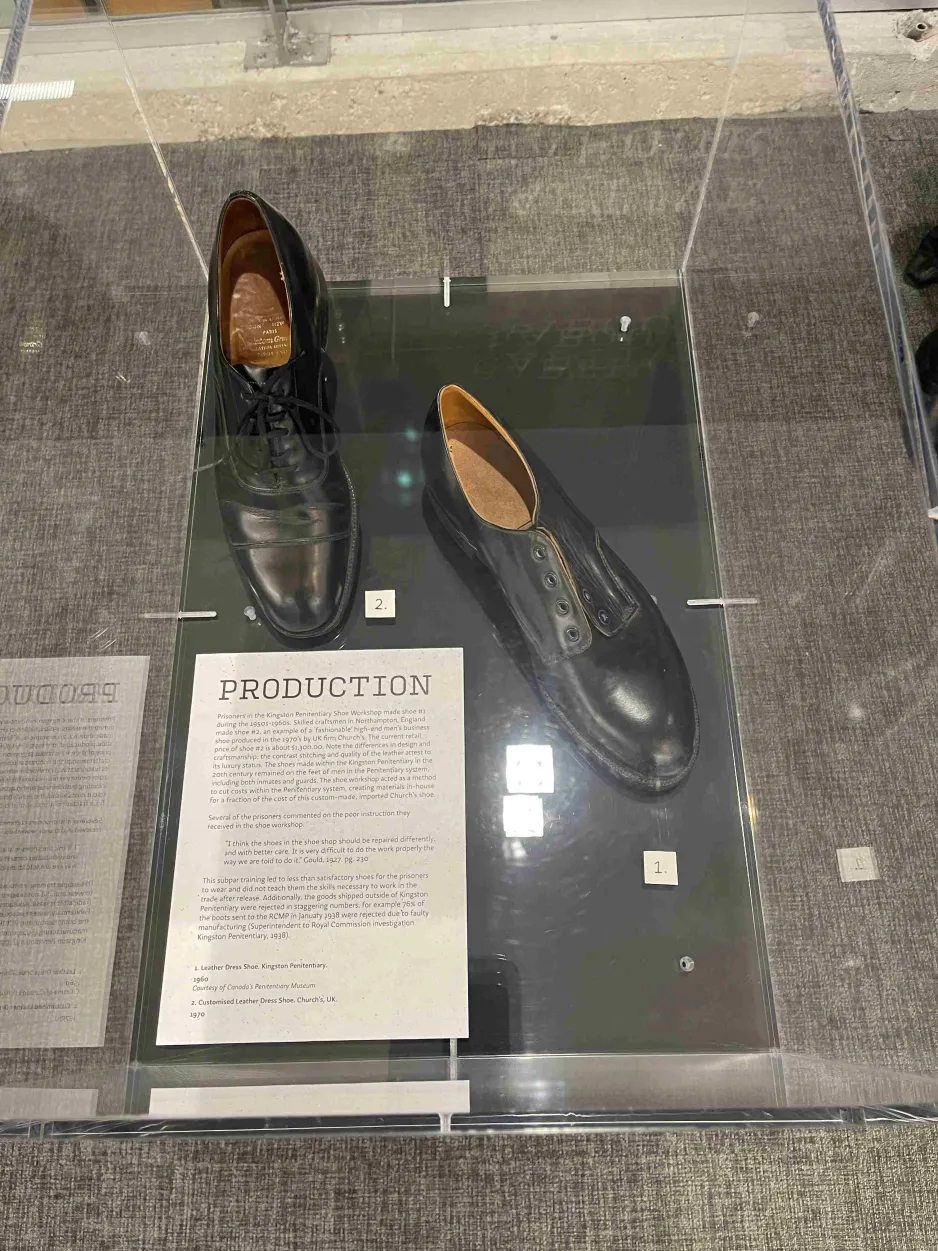 A small exhibition display case containing two mismatched black leather shoes.