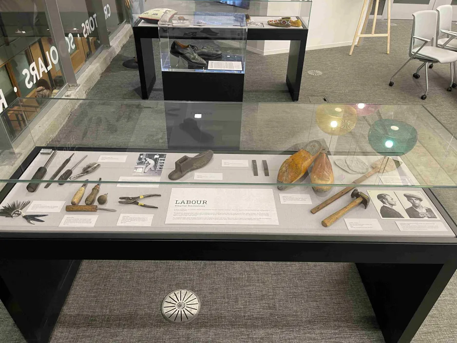 An exhibition display case in which shoe making hand tools, shoe lasts, and a fly swatter are visible.