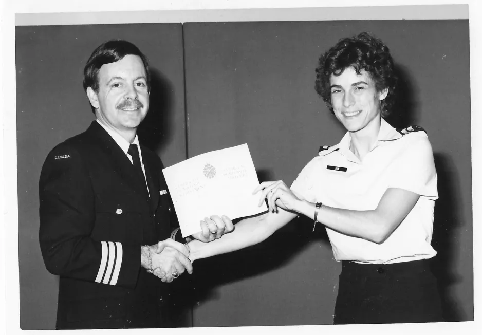 A black-and-white photo of a smiling serviceman and servicewoman shaking hands, as the man hands the woman a certificate.