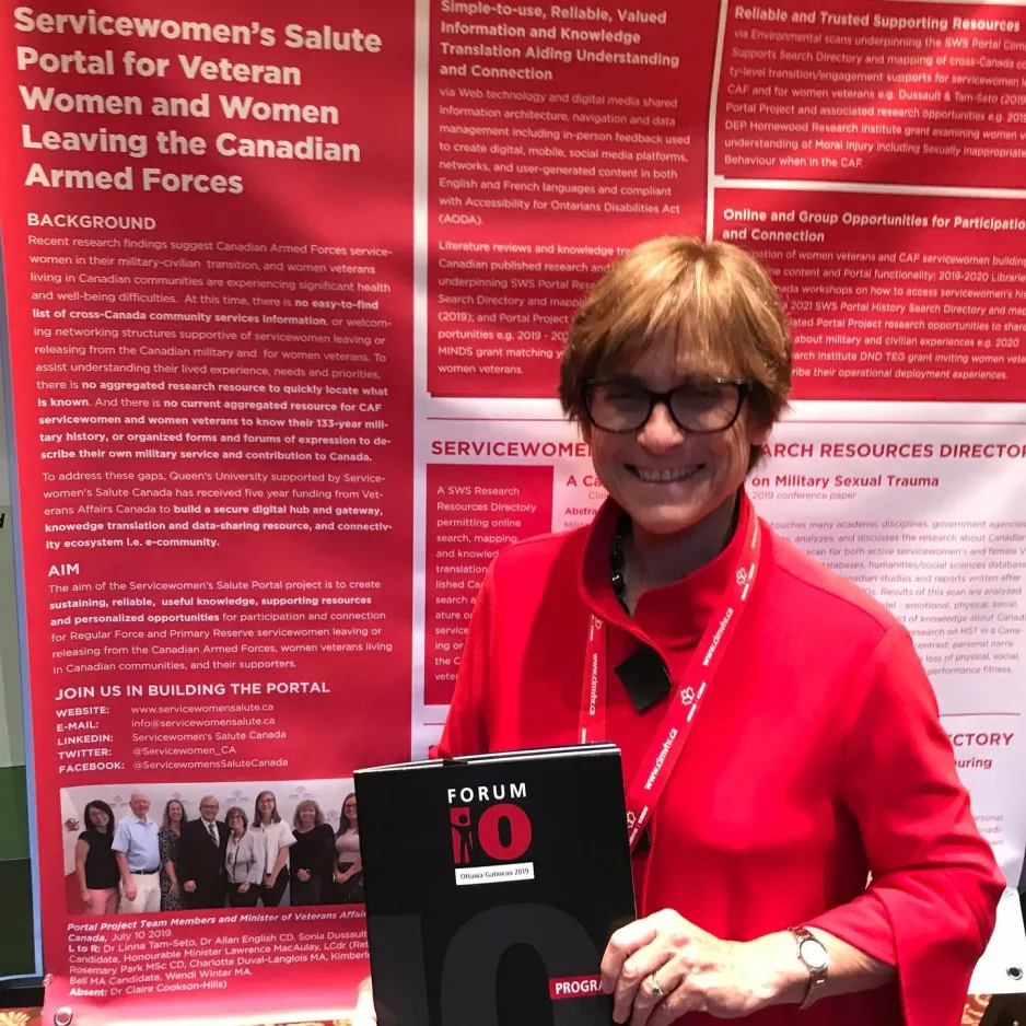 A smiling woman in red clothing poses with a booklet in front of a red and white conference poster.