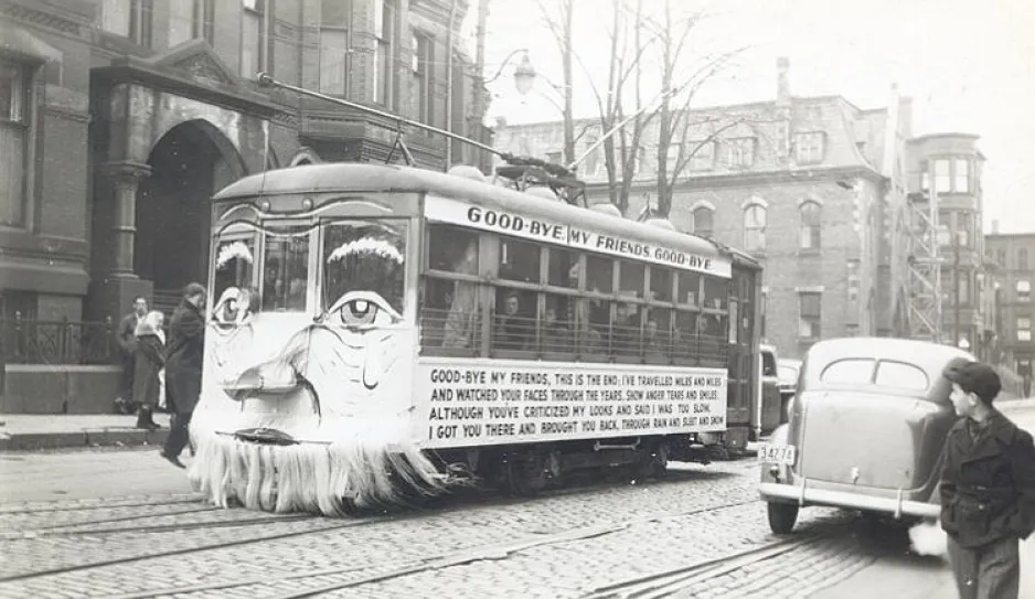 A black and white photograph of a streetcar, decorated with a face and a poem. The poem begins: “Good-bye my friends good-bye.”