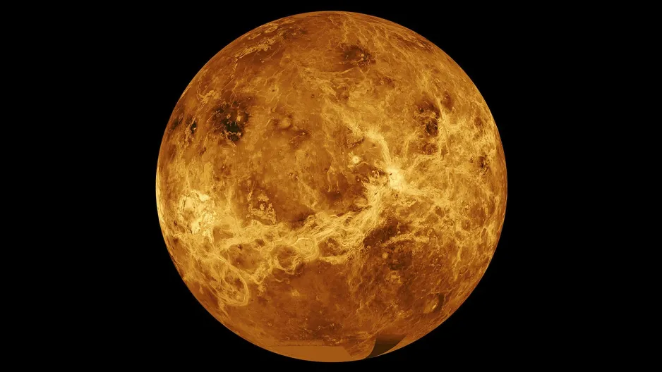 Une carte radar illustrant un côté de la surface de Vénus, où elle est de couleur jaune-orange à orange-brun, avec une variété de caractéristiques circulaires, linéaires et irrégulières, mais aucune facilement identifiable à l'exception de quelques cratères. La région du pôle sud est de couleur beige en raison d’un manque de données - sur un fond noir représentant l'espace.