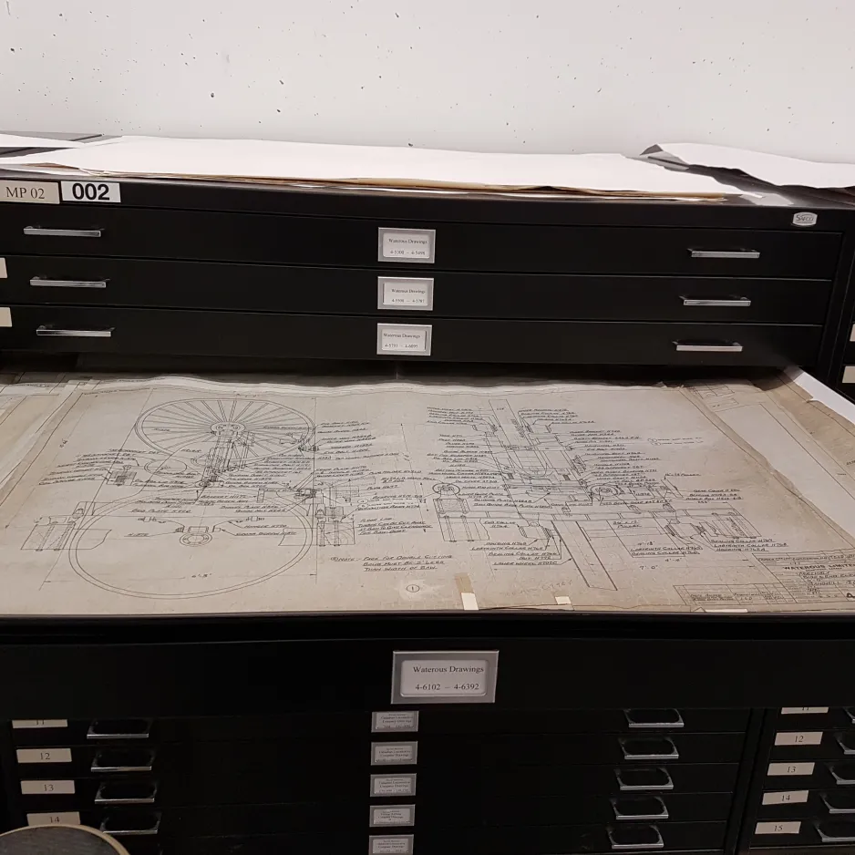 Colour photo shows the drawer of a black flat-storage or map cabinet extended.  In the drawer is a technical drawing of a bandmill double cutting saw. 