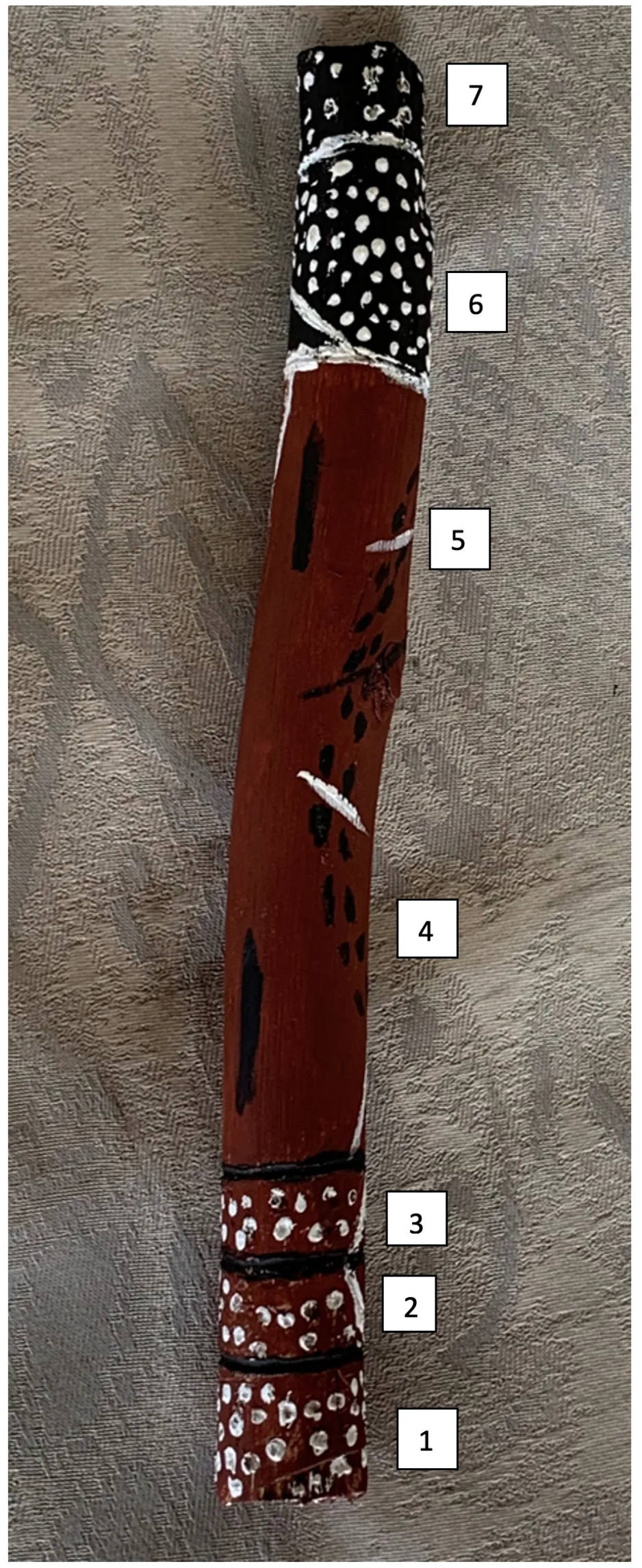 Stick used for cultural purposes painted with brown, white, and black markings.