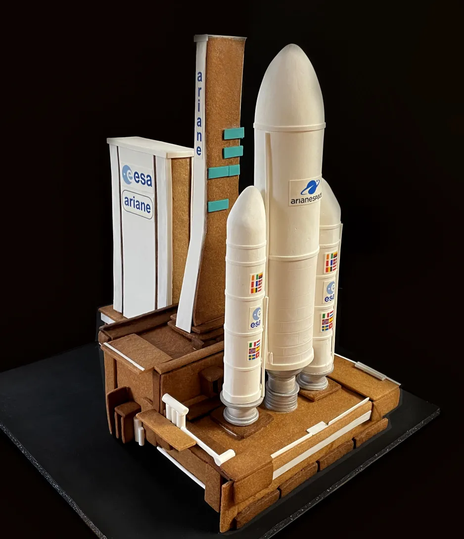 A gingerbread and sugar model of the Ariane 5 launch vehicle is pictured against a dark backdrop.